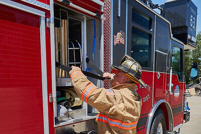 A firefighter at an emergency scene opens a compartment roll-up door to access equipment inside. 